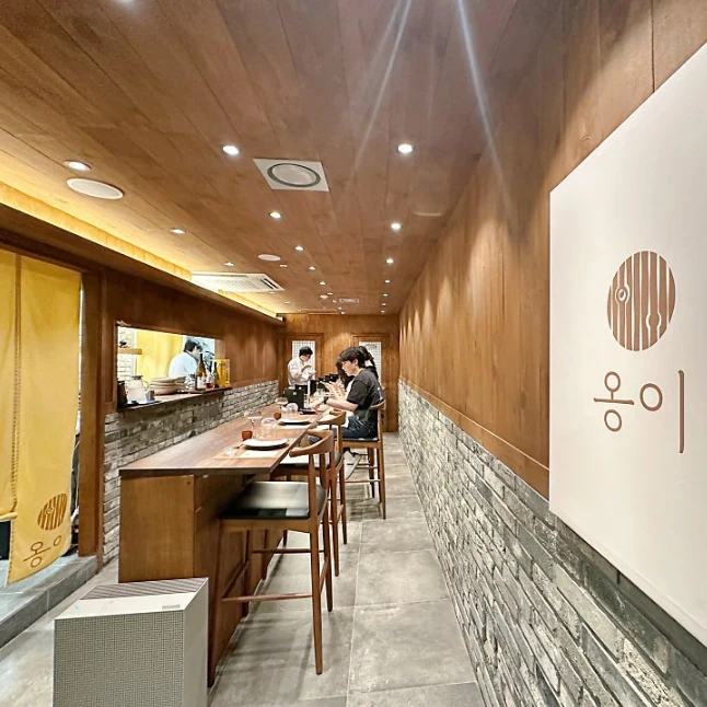 옹이 매장 내부 — 원목 천장과 벽, 회색 석벽, 원목 바 카운터와 옹이 로고 사인